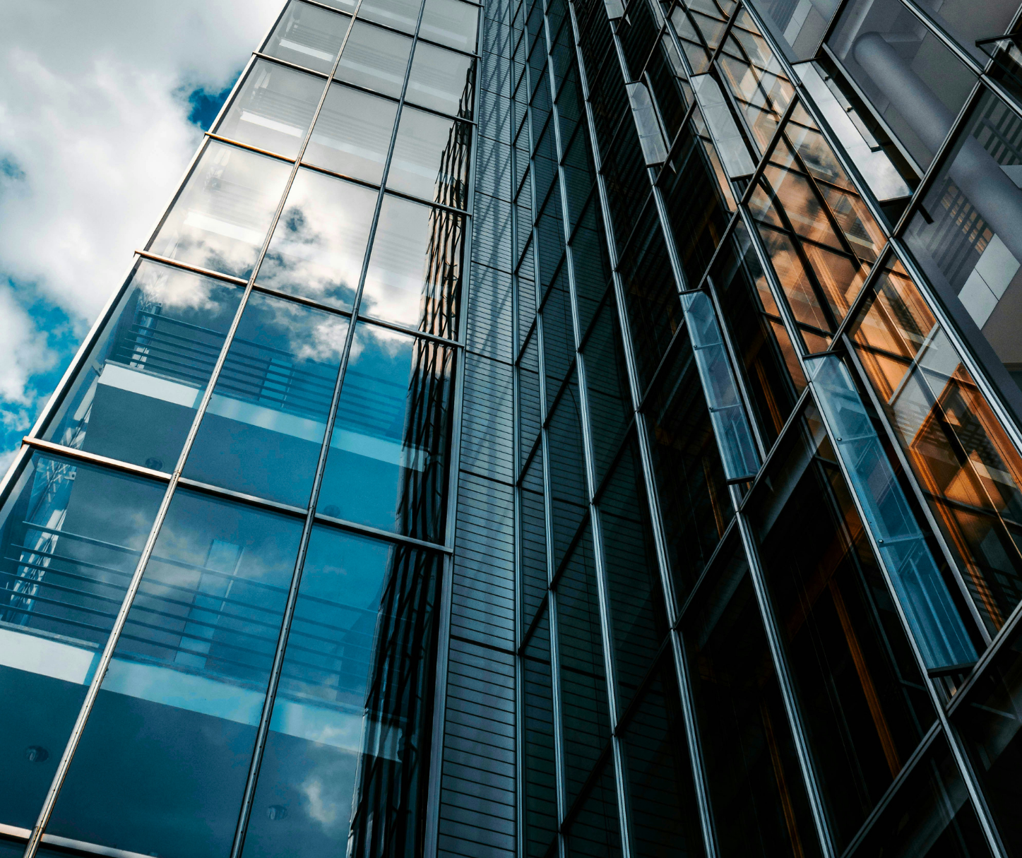 A tall modern glass building reflecting the sky and clouds.