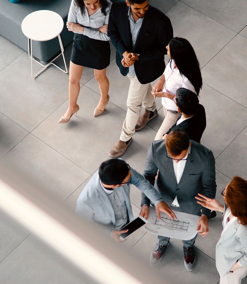 A group of five professionals, three men and two women, gathered around a table looking at a blueprint or architectural plan in a modern office setting.