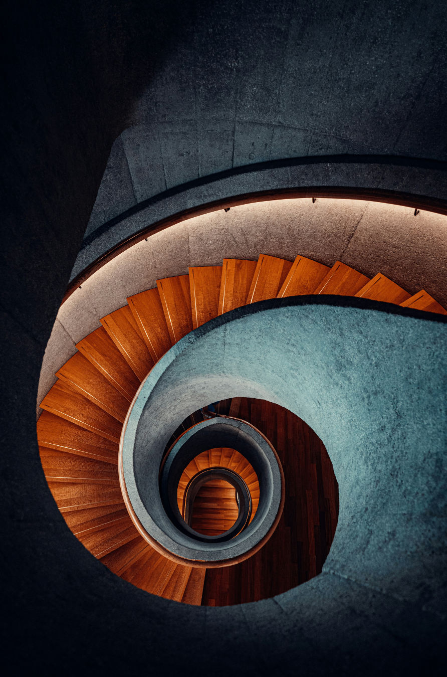 Top view of a spiral staircase with wooden steps and concrete walls.