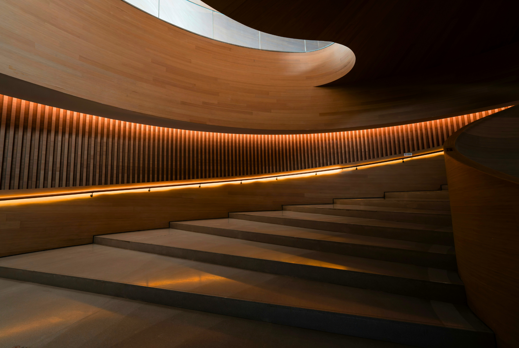 Modern interior with wooden curved walls, soft lighting, and stairs.