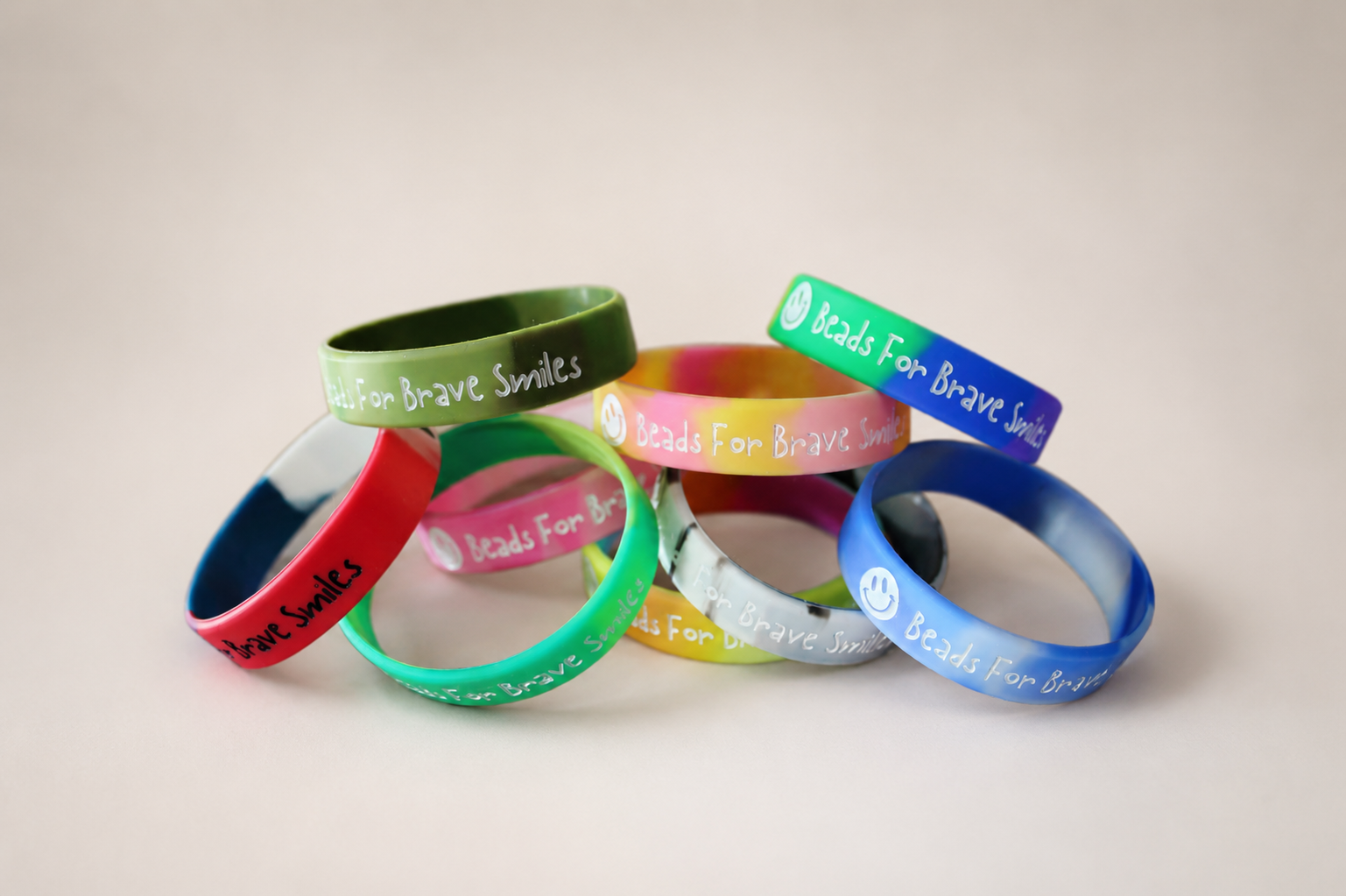 Colorful silicone wristbands with the inscription 'Beads For Brave Smiles' and a smiley face, arranged on a white surface.