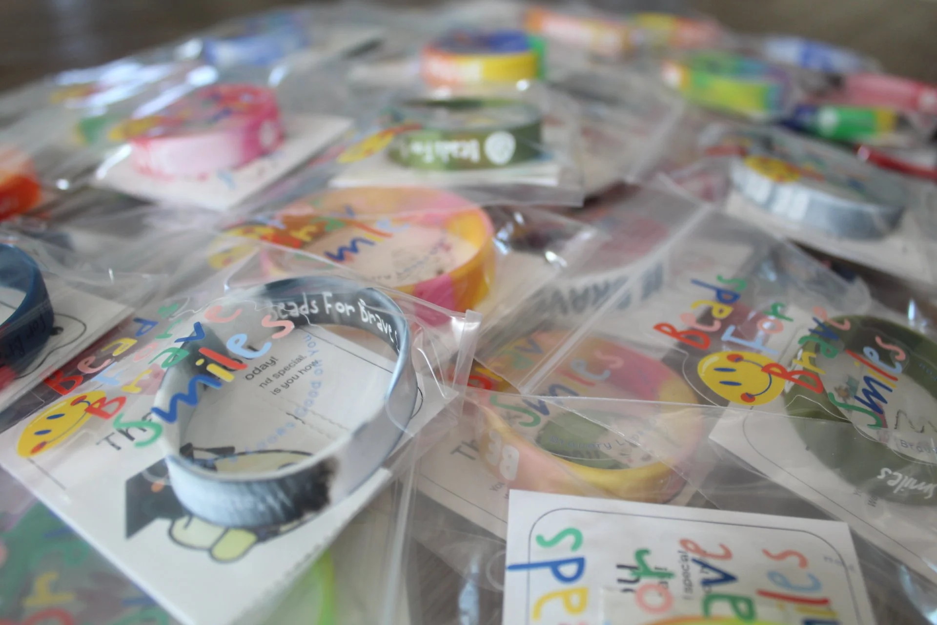 Multiple small plastic bags containing colorful wristbands with rainbow colors and smiley faces, scattered on a surface.