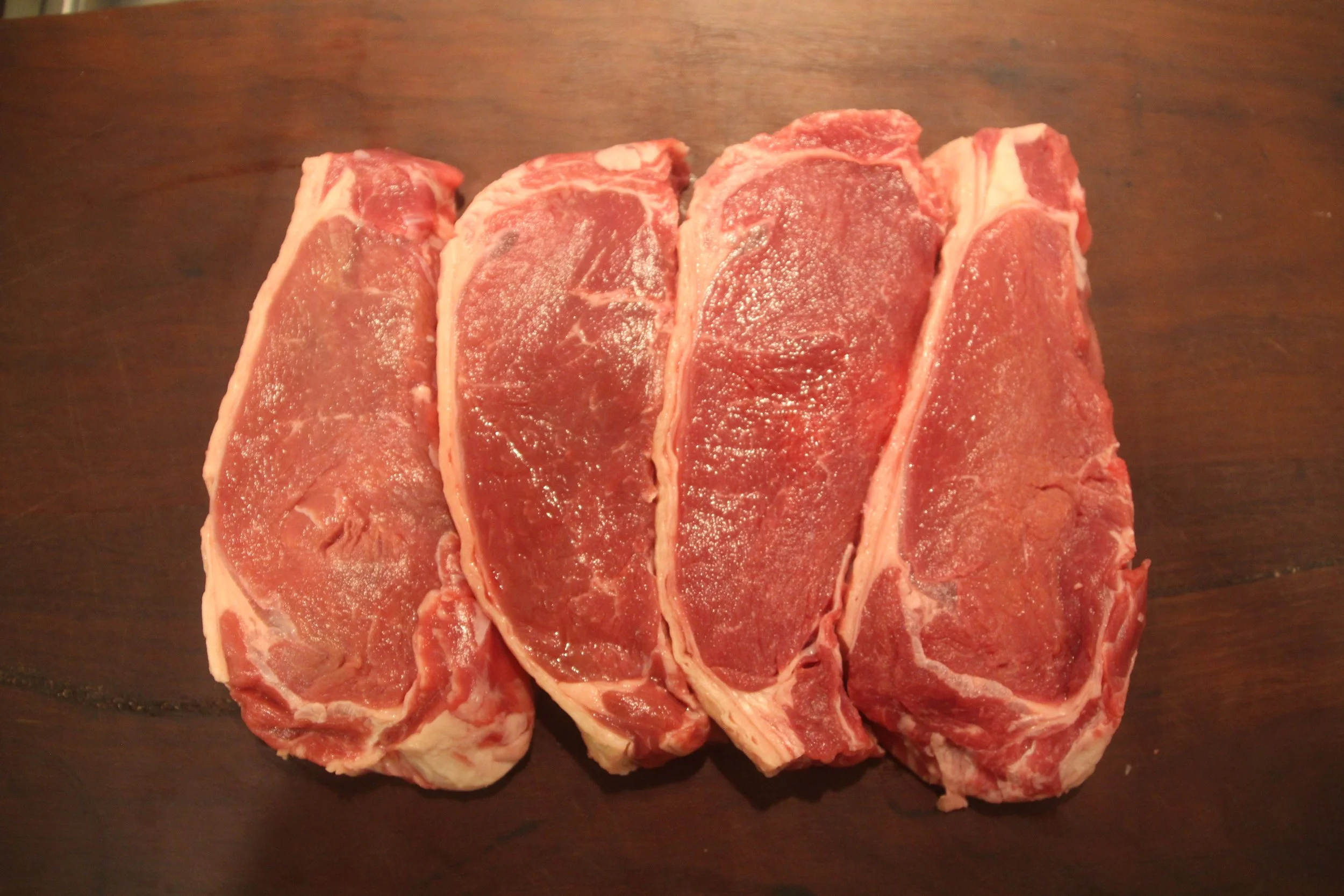 Four steak cuts on a dark wooden surface.