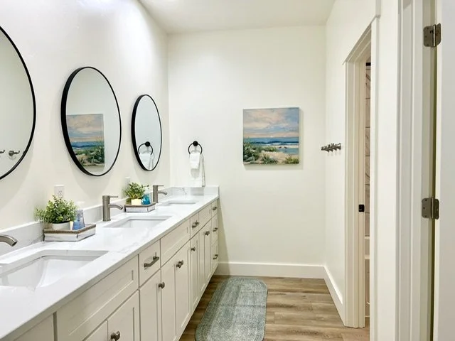 Bathroom with three sinks, mirrors, and wall art depicting a beach scene.
