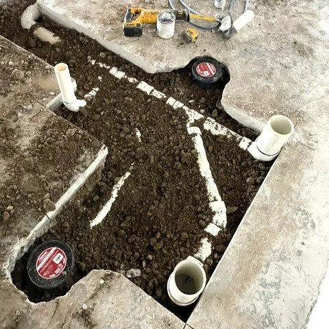 Underground plumbing pipes with dirt surroundings and construction tools nearby.