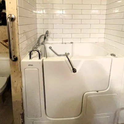 A white bathtub with a handheld showerhead and grab bars in a bathroom with tiled walls.