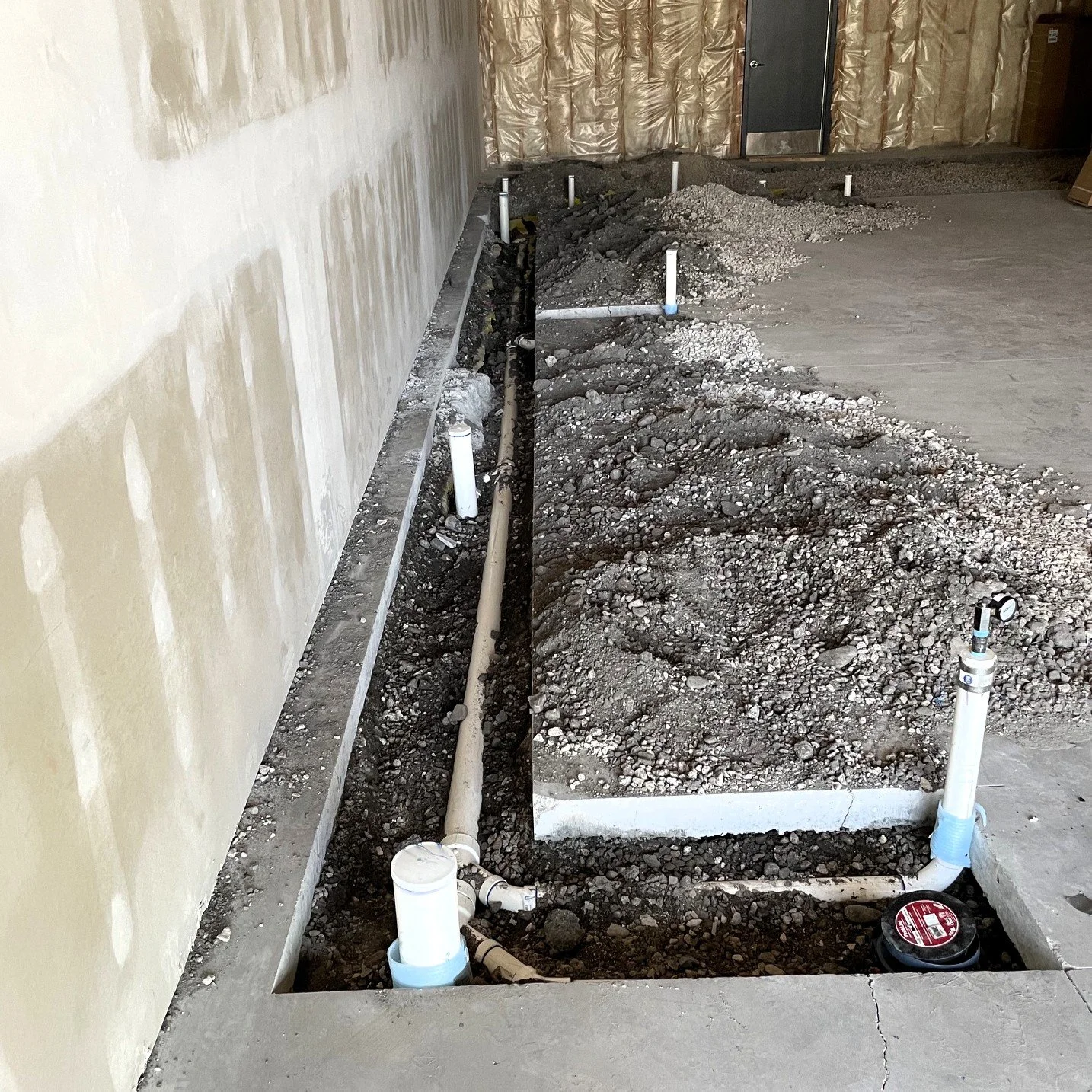 Construction site with exposed pipes and gravel in a partially finished room.