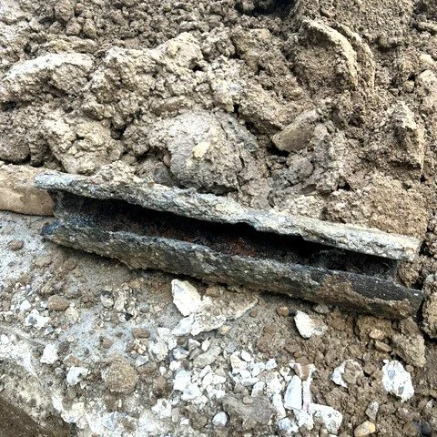 Close-up view of a damaged metal pipe or conduit buried in soil and surrounded by dirt and rocks.