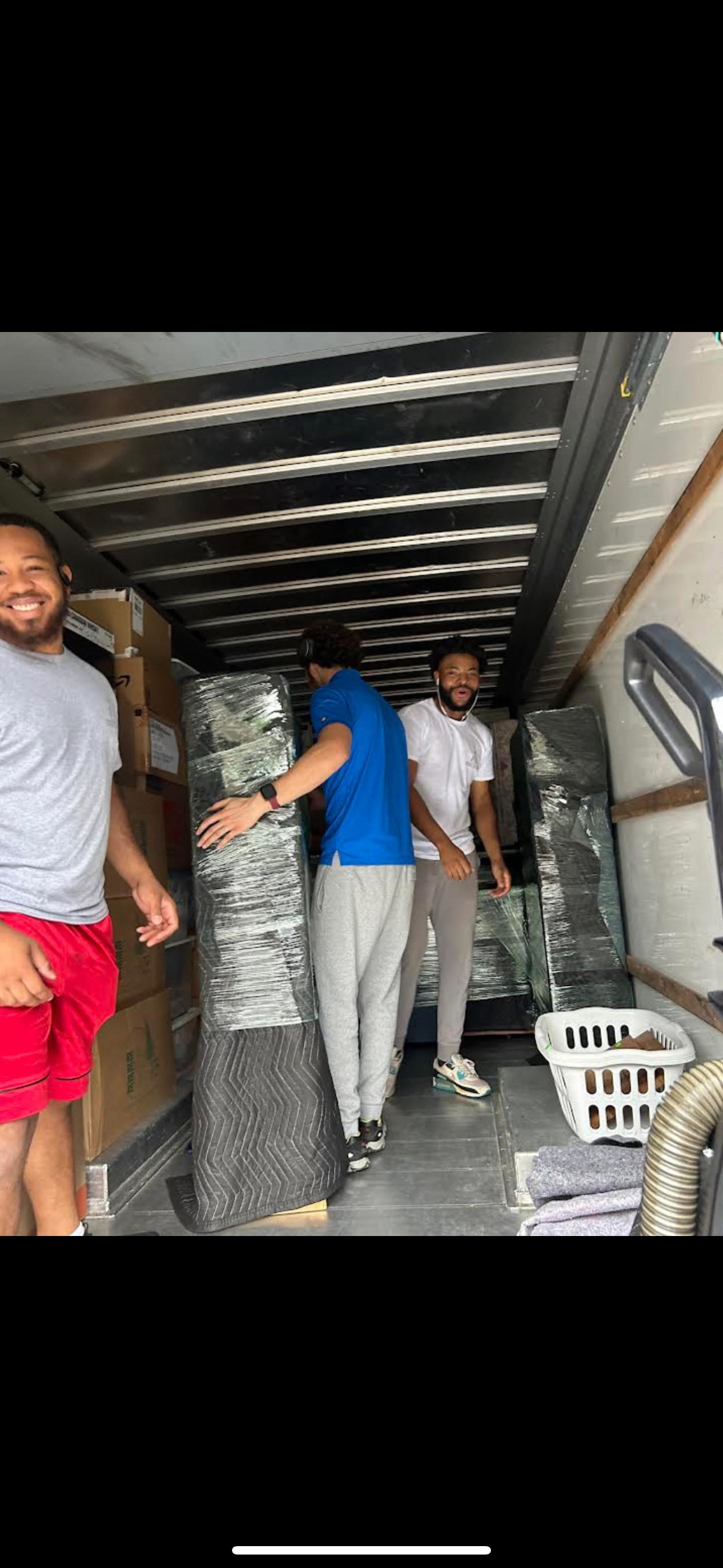 A picture of 3 male professional movers loading wrapped items into a moving truck.