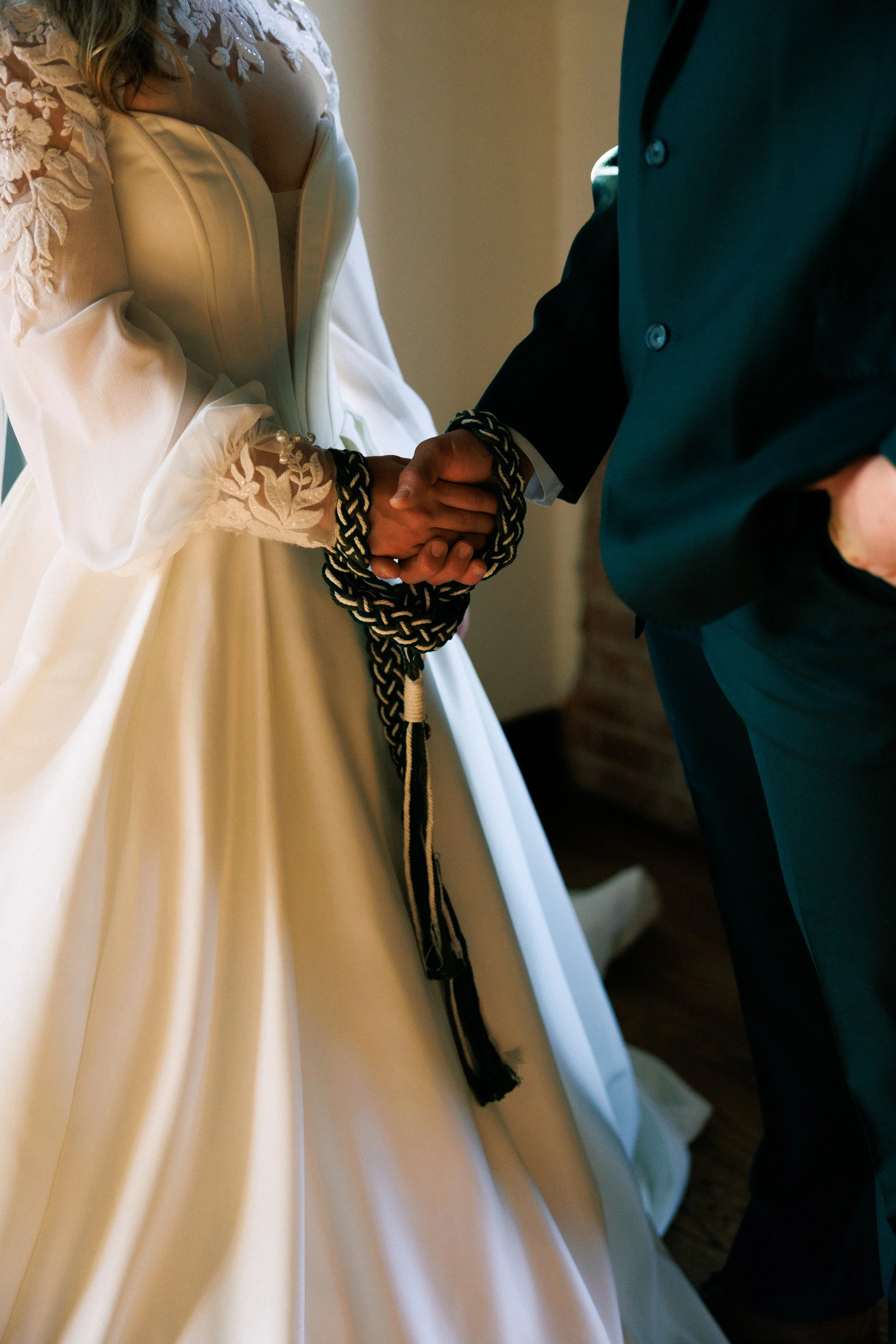Close-up of two people shaking hands, one dressed in a wedding gown with lace details, the other in a dark suit.