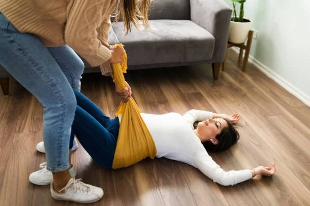 Person in yellow shirt pulling another person in white shirt and blue jeans on the floor in a living room.