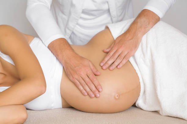 A medical professional performing abdominal massage on a pregnant woman lying on her side.