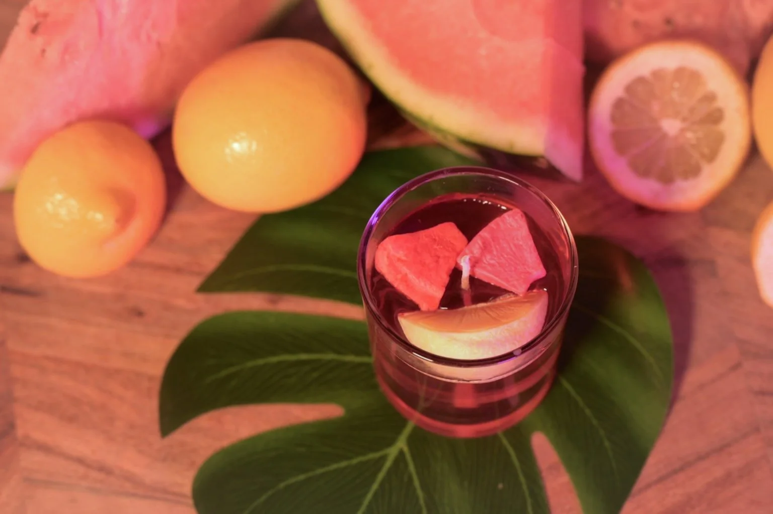 Curious Confections Pink Watermelon Lemonade candle surrounded by fresh watermelon and citrus, highlighting its vibrant summer-inspired fragrance profile.