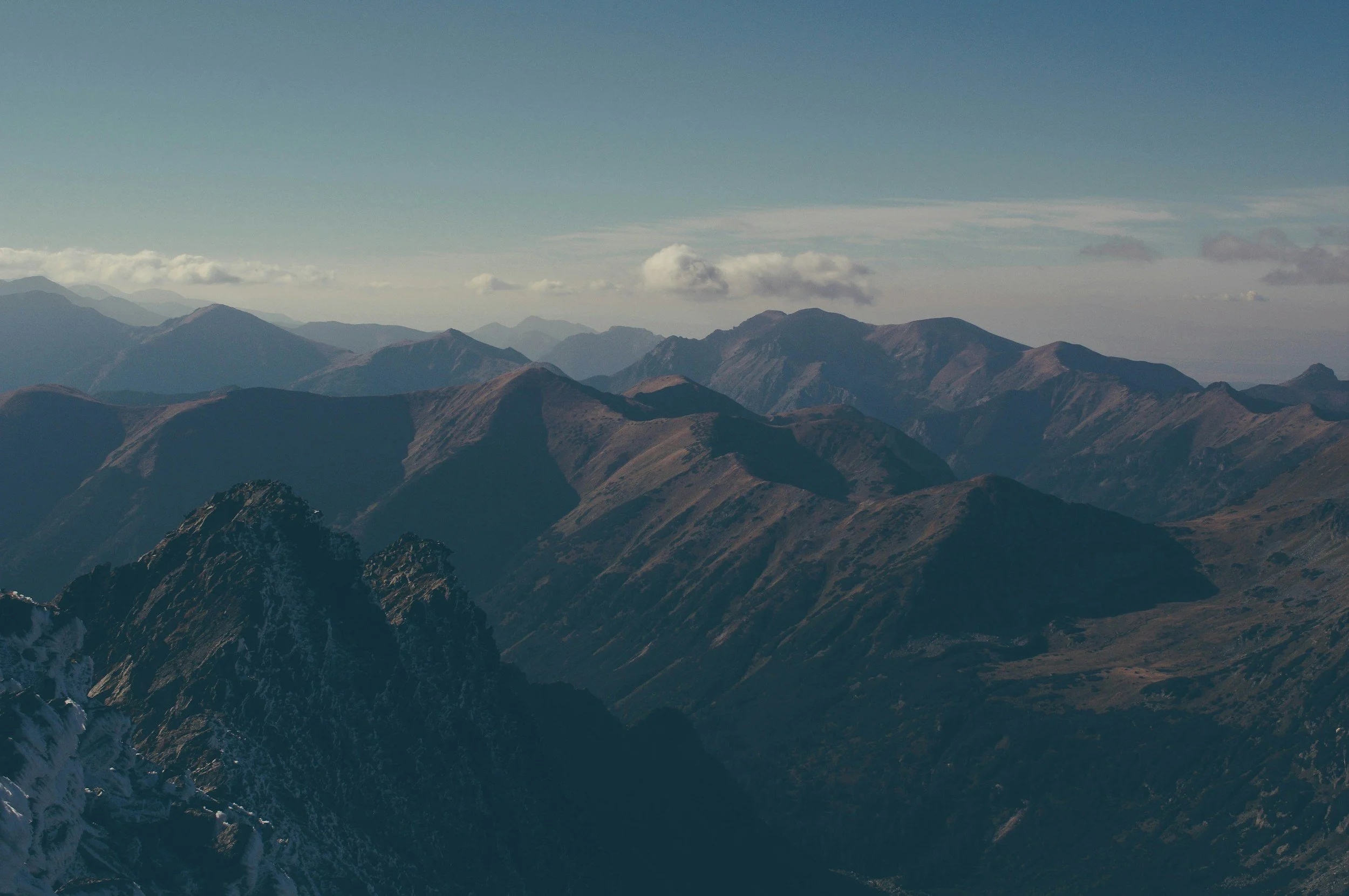 Scenic view of a mountain range with rugged peaks and some snow patches, under a blue sky with scattered clouds.