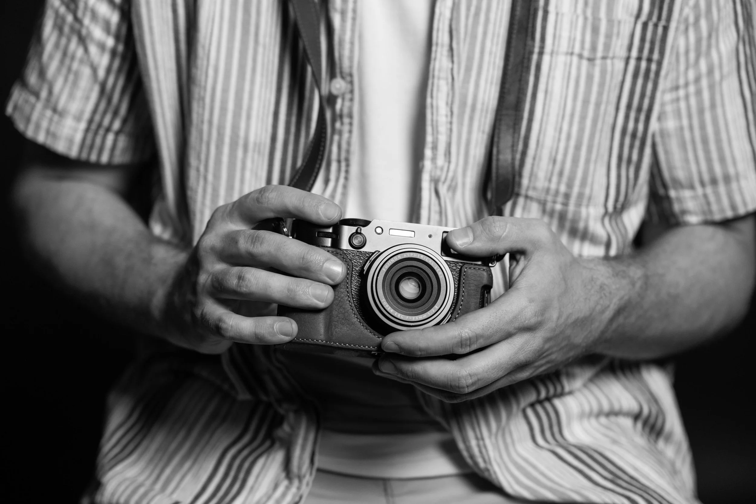 Close-up of a person holding a camera, with a striped shirt visible in black and white.