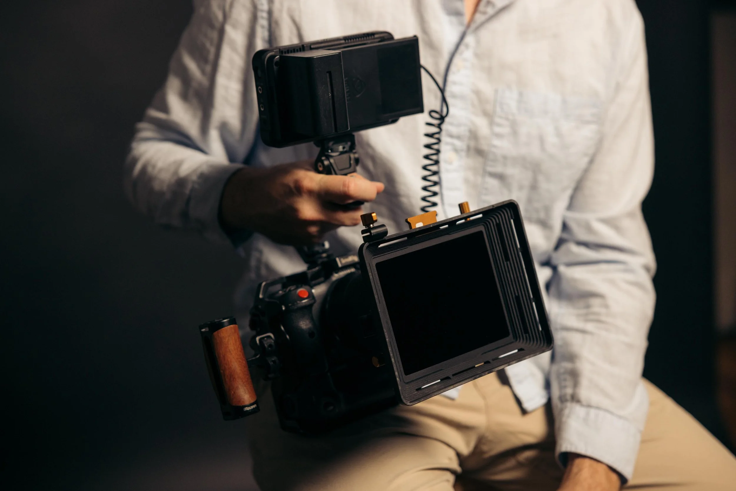 A person holding a professional camera rig with a mounted camera and accessories, wearing a light-colored shirt and pants.
