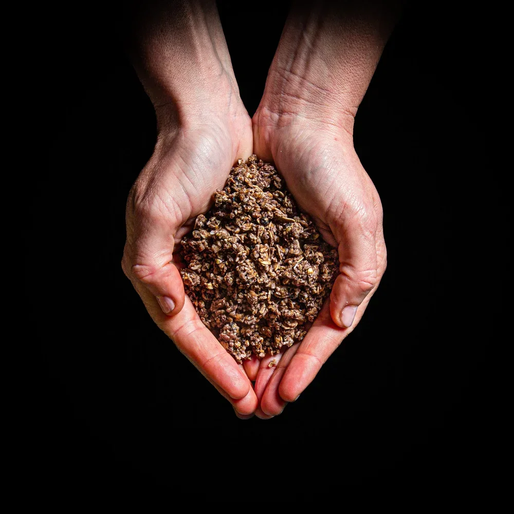 Hands holding a pile of crushed chocolate cookies against a black background.