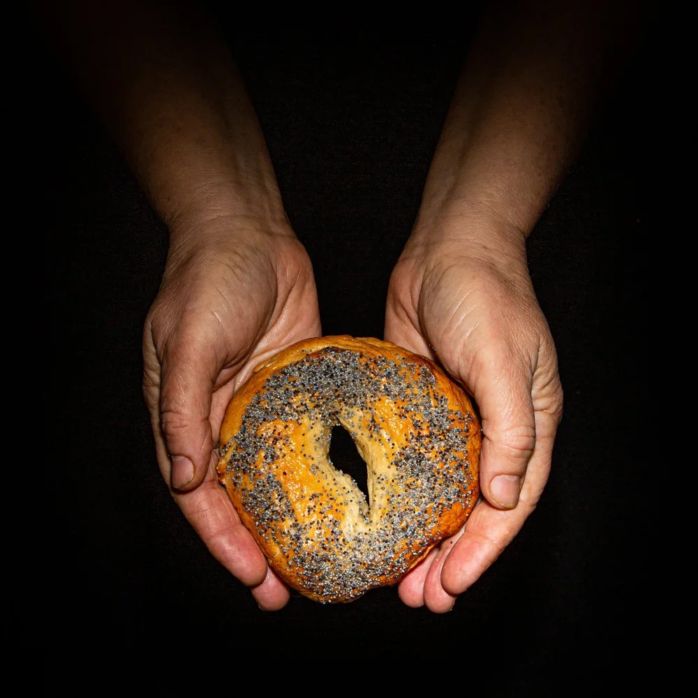 Two hands holding a sprinkled bagel with a hole in the center against a black background.