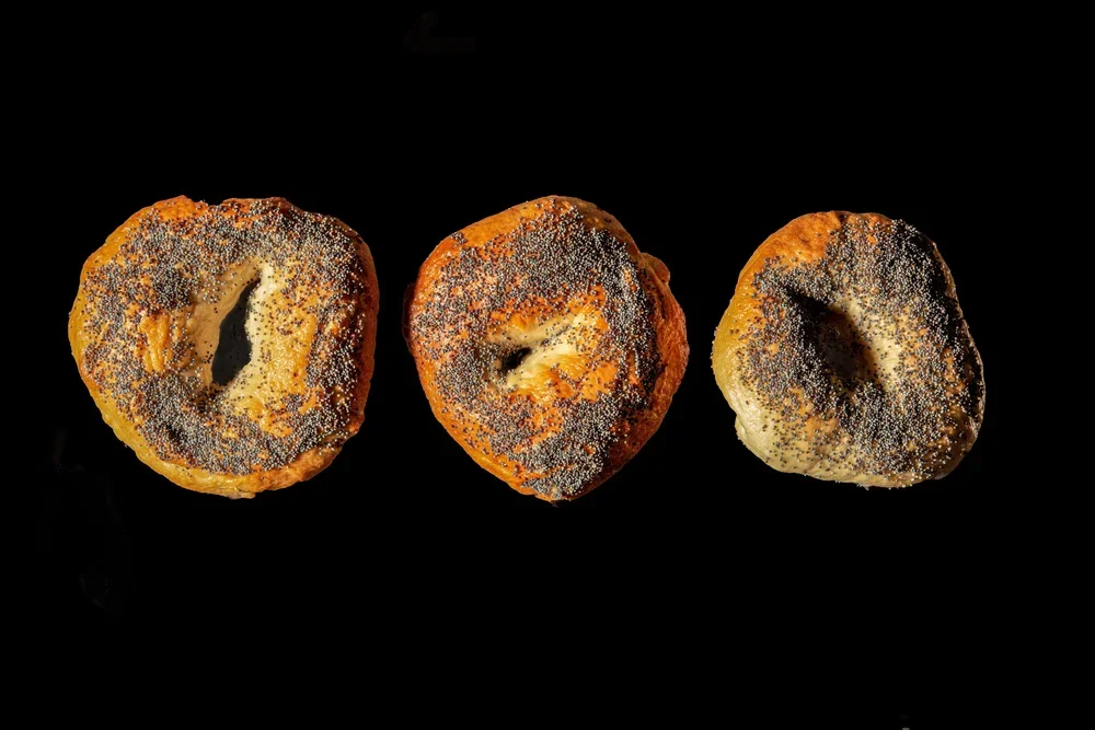 Three bagels with poppy seeds on top, arranged in a row on a black background.