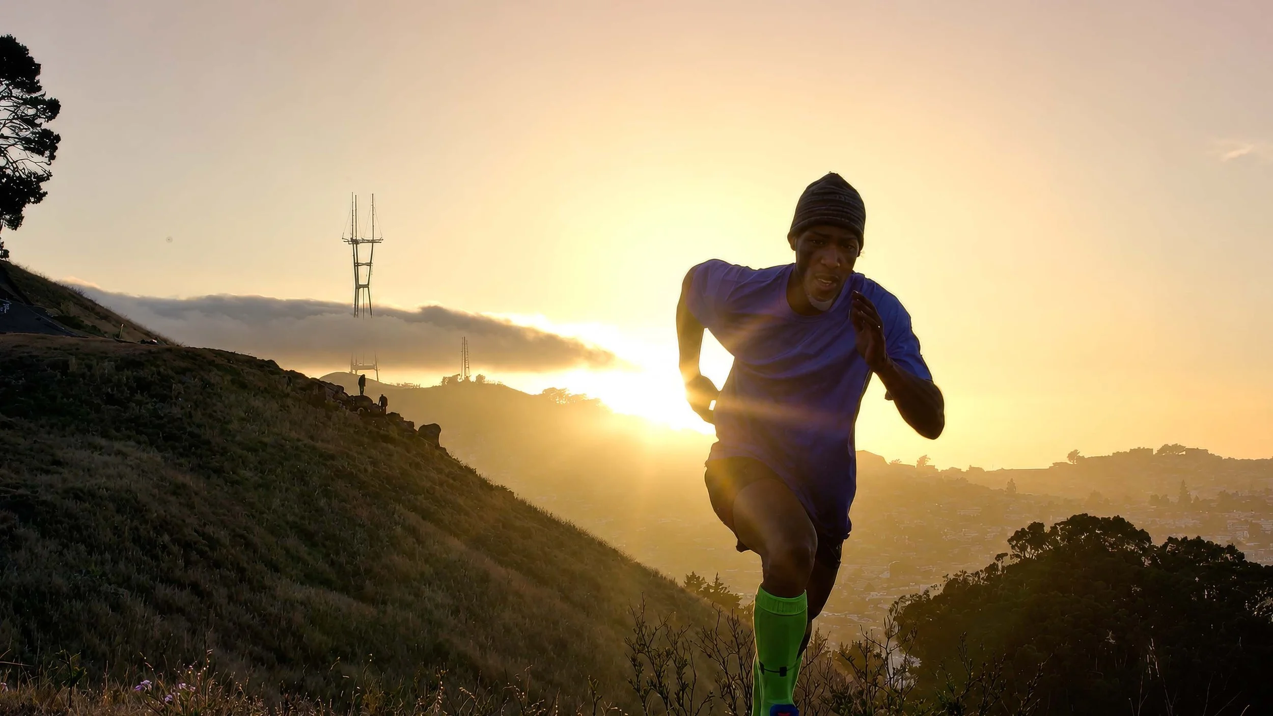Runner wearing a beanie and neon green socks running in a natural landscape at sunset.