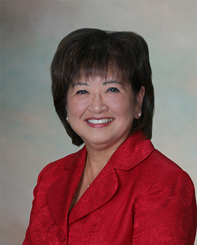 A woman in a red blazer smiling against a gray background.