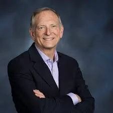 Portrait of a smiling man in a dark suit with crossed arms, against a dark background.