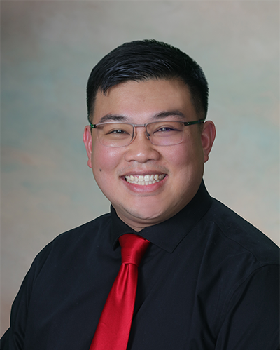Portrait of a smiling man with glasses, wearing a black shirt and red tie, against a neutral background.
