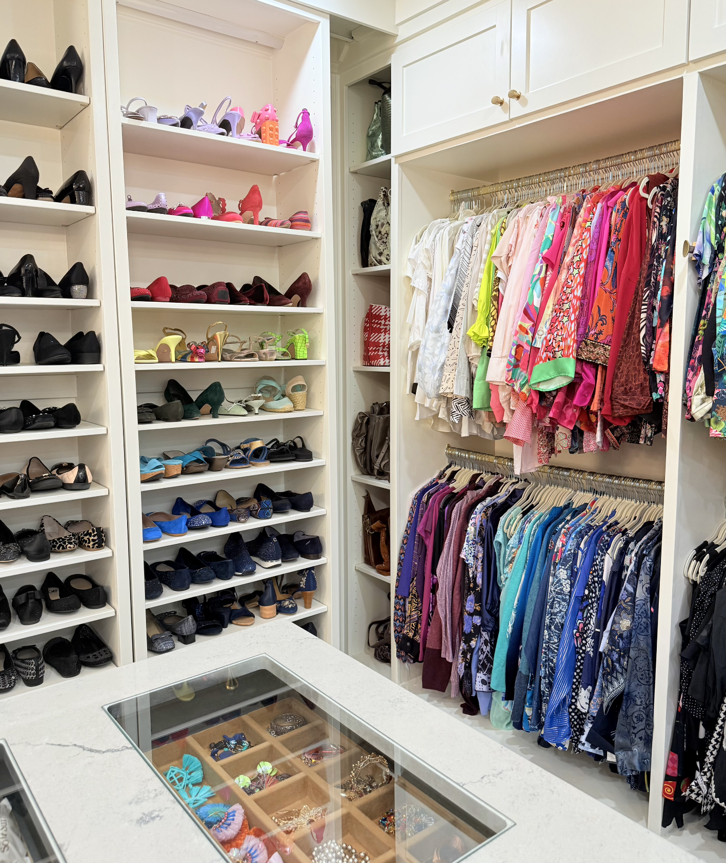 A closet with white shelves filled with colorful shoes and clothing racks with assorted dresses, tops, and skirts.