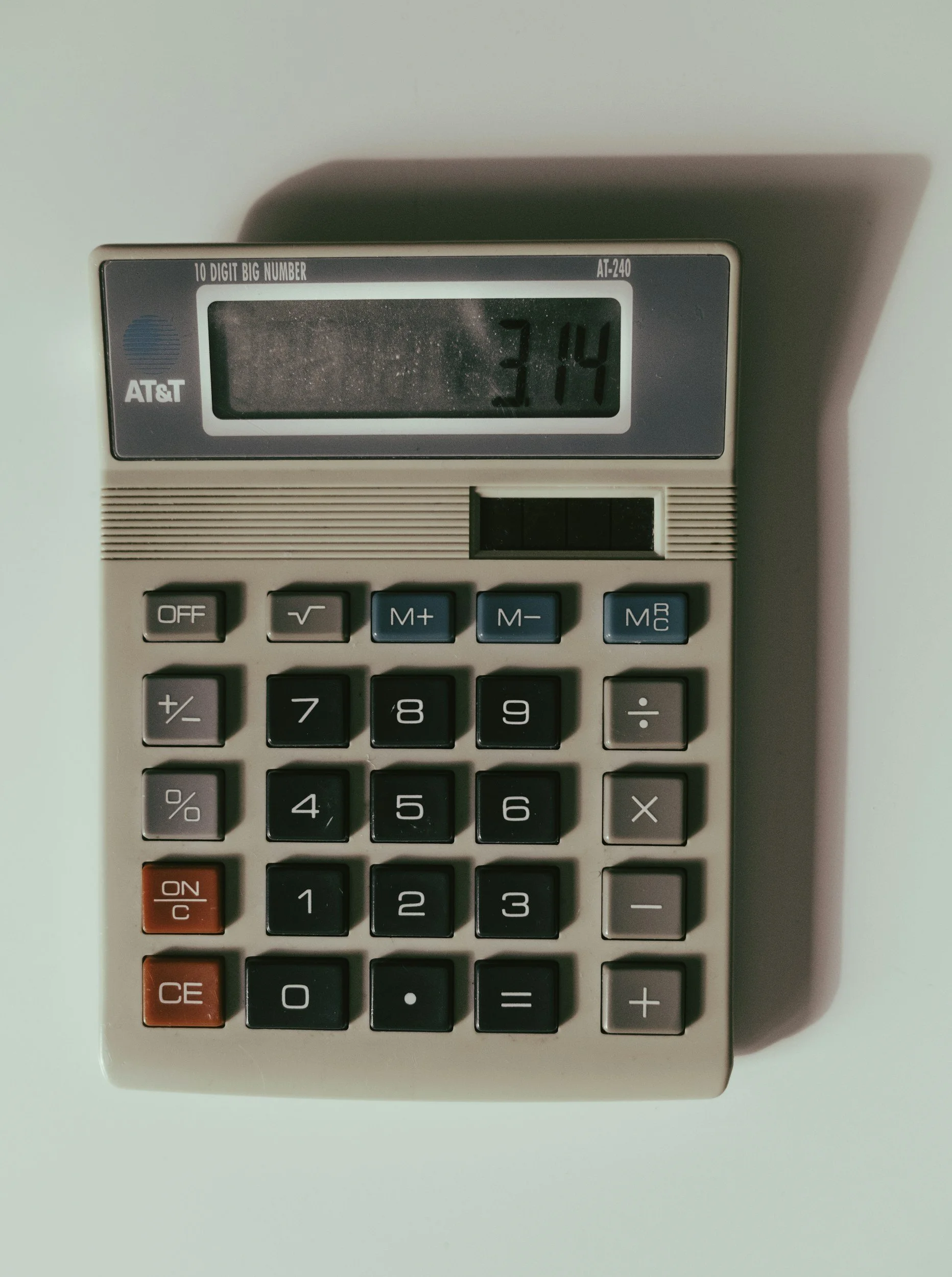 A gray calculator with black and red buttons showing the time 3:14 on its display.