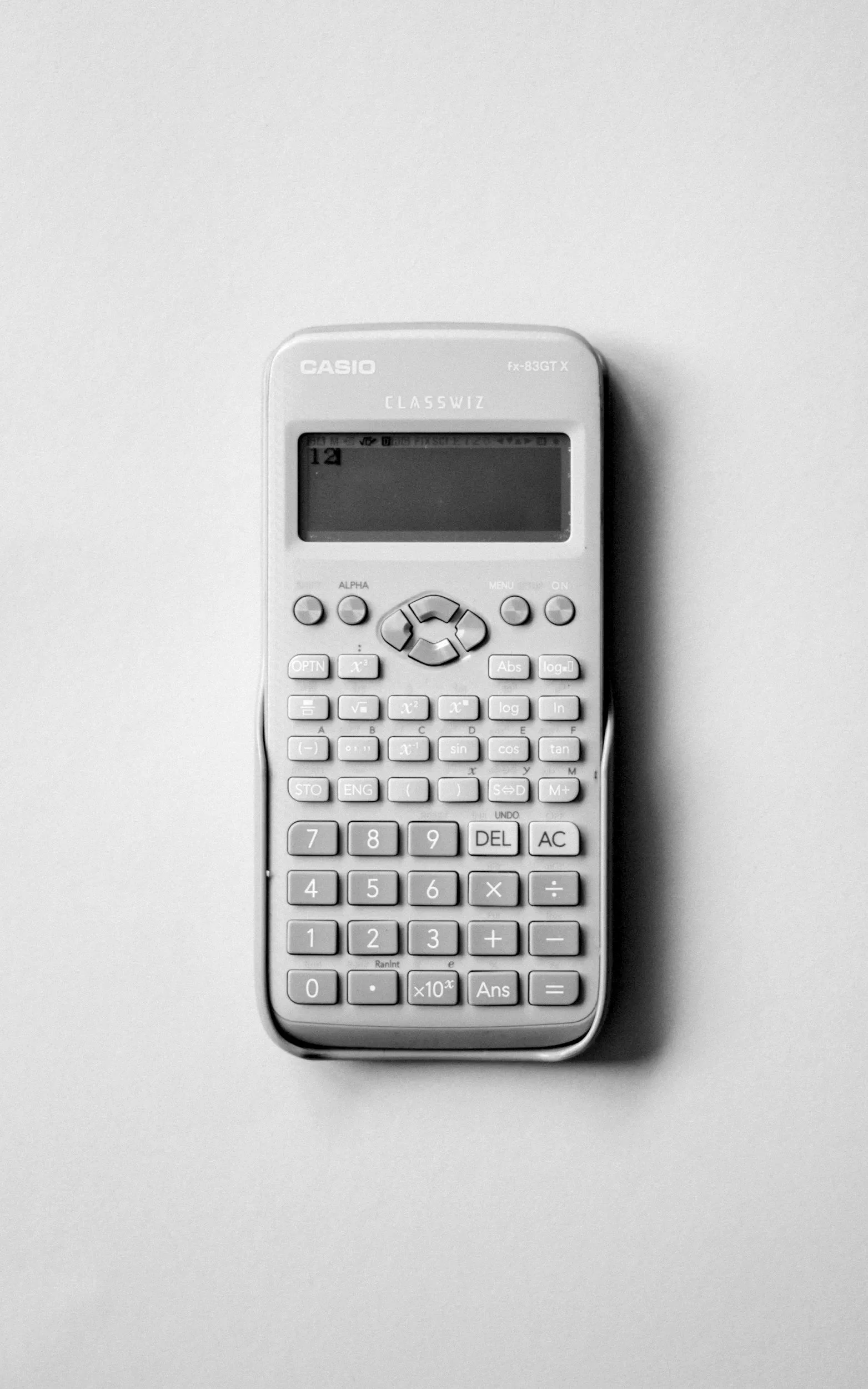 A white calculator with a digital display and numerous buttons placed on a light-colored surface.
