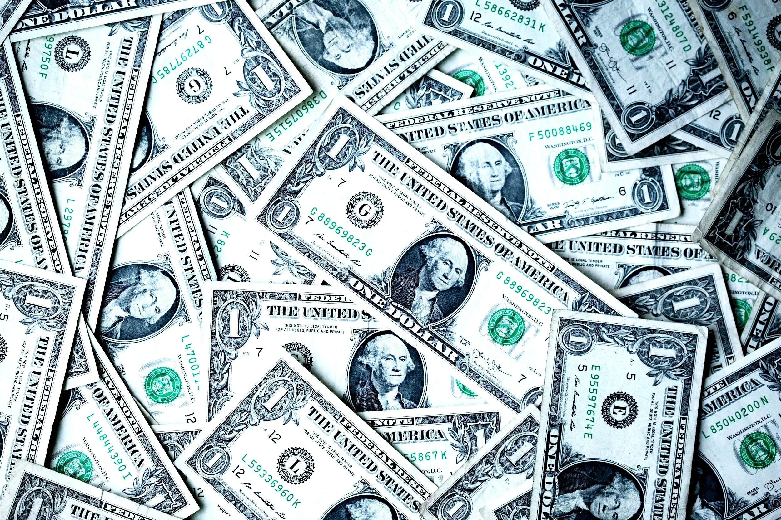 A pile of one-dollar US bills scattered randomly.
