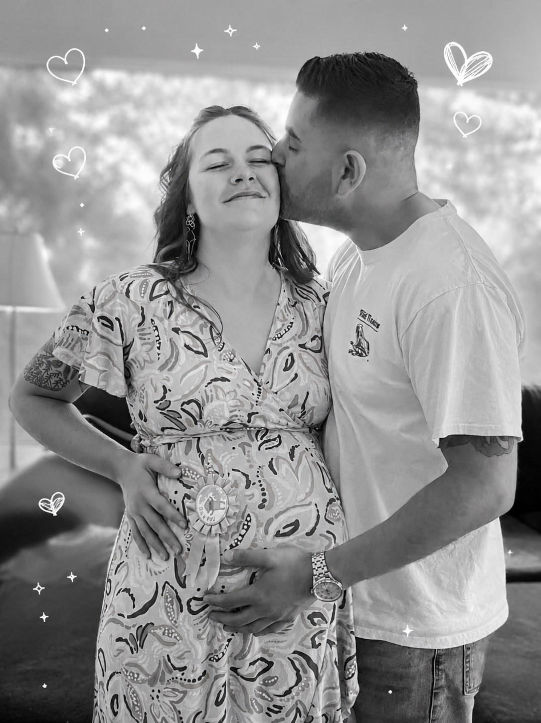 A pregnant woman with a ribbon badge on her dress, smiling with her eyes closed, while a man kisses her on the forehead, both holding her belly, in a cozy indoor setting decorated with hand-drawn hearts and stars.