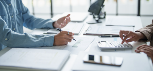 Two people sitting at a table with documents and a calculator, discussing or working on financial or business matters.
