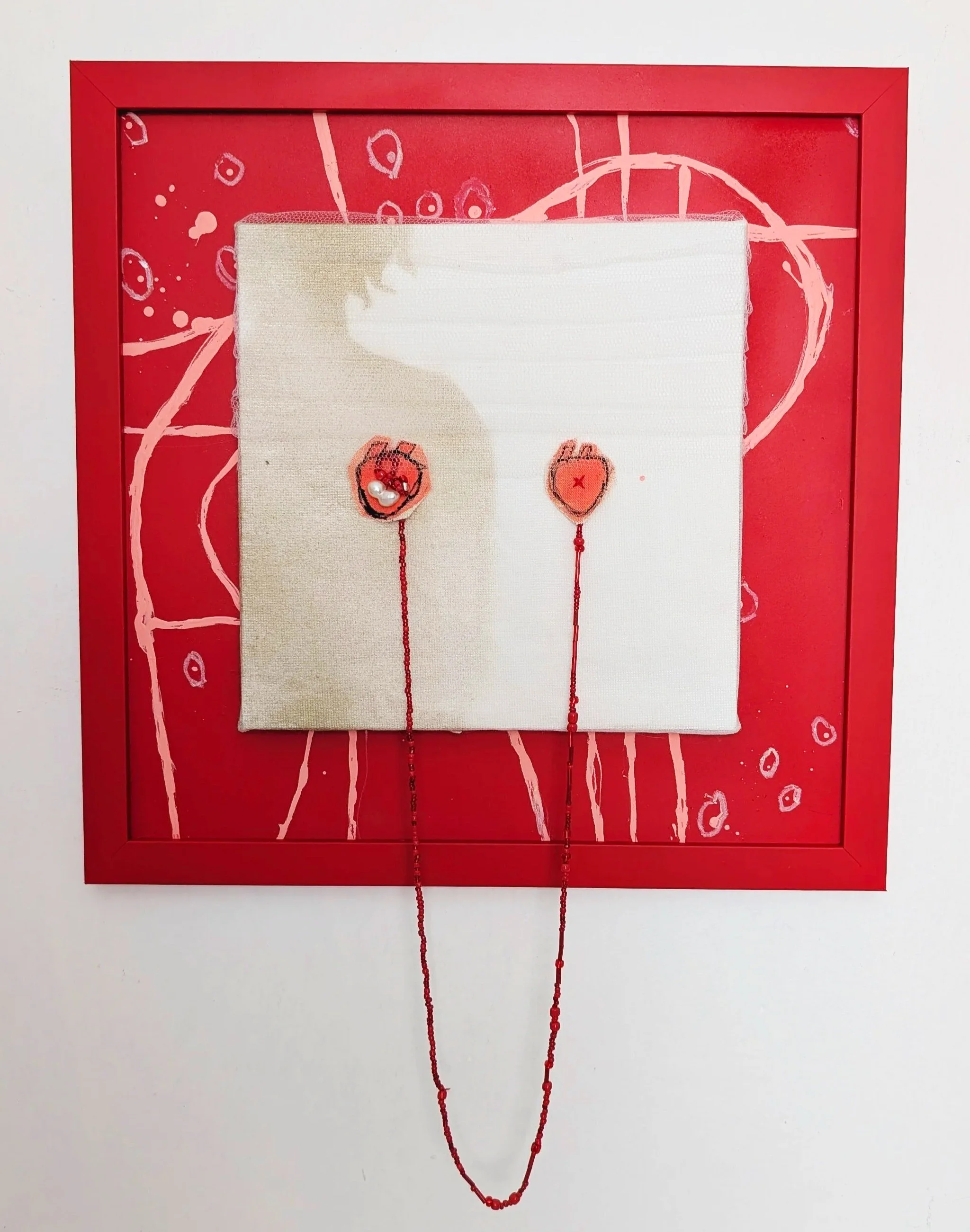 An expressive piece: canvas with hand-stitched art of two hearts connected by a string, displayed against a red background with pink abstract scribbles and dots, framed in a red border.