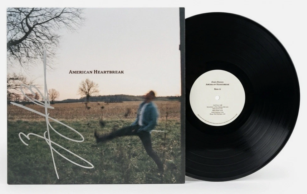 A vinyl record and album cover titled 'American Heartbreak'. The album cover shows a blurred person jumping in a field with trees and a sunset in the background.