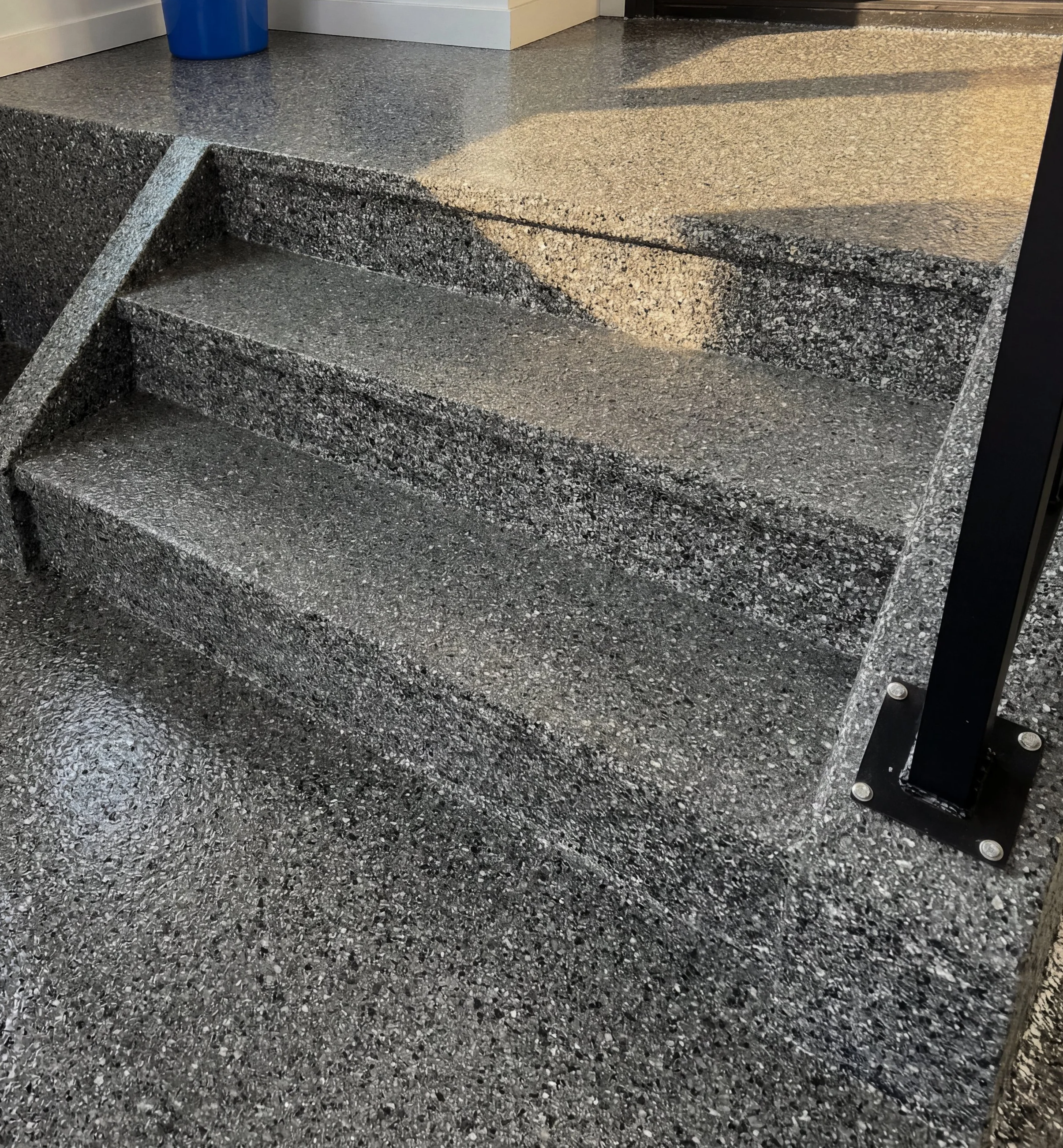Epoxy stairs leading up to a higher level, with a black metal railing on the right side.