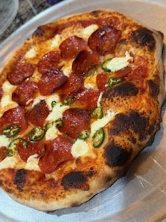A pepperoni and cheese pizza with tomato sauce and green pepper slices in a cardboard pizza box.