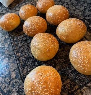 A wire cooling rack with freshly baked round bread rolls sprinkled with salt.
