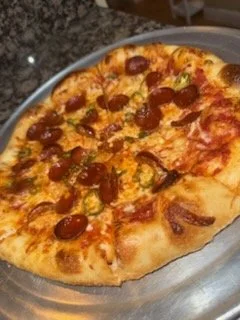 A pepperoni pizza on a round tray, topped with cheese and pepperoni slices.