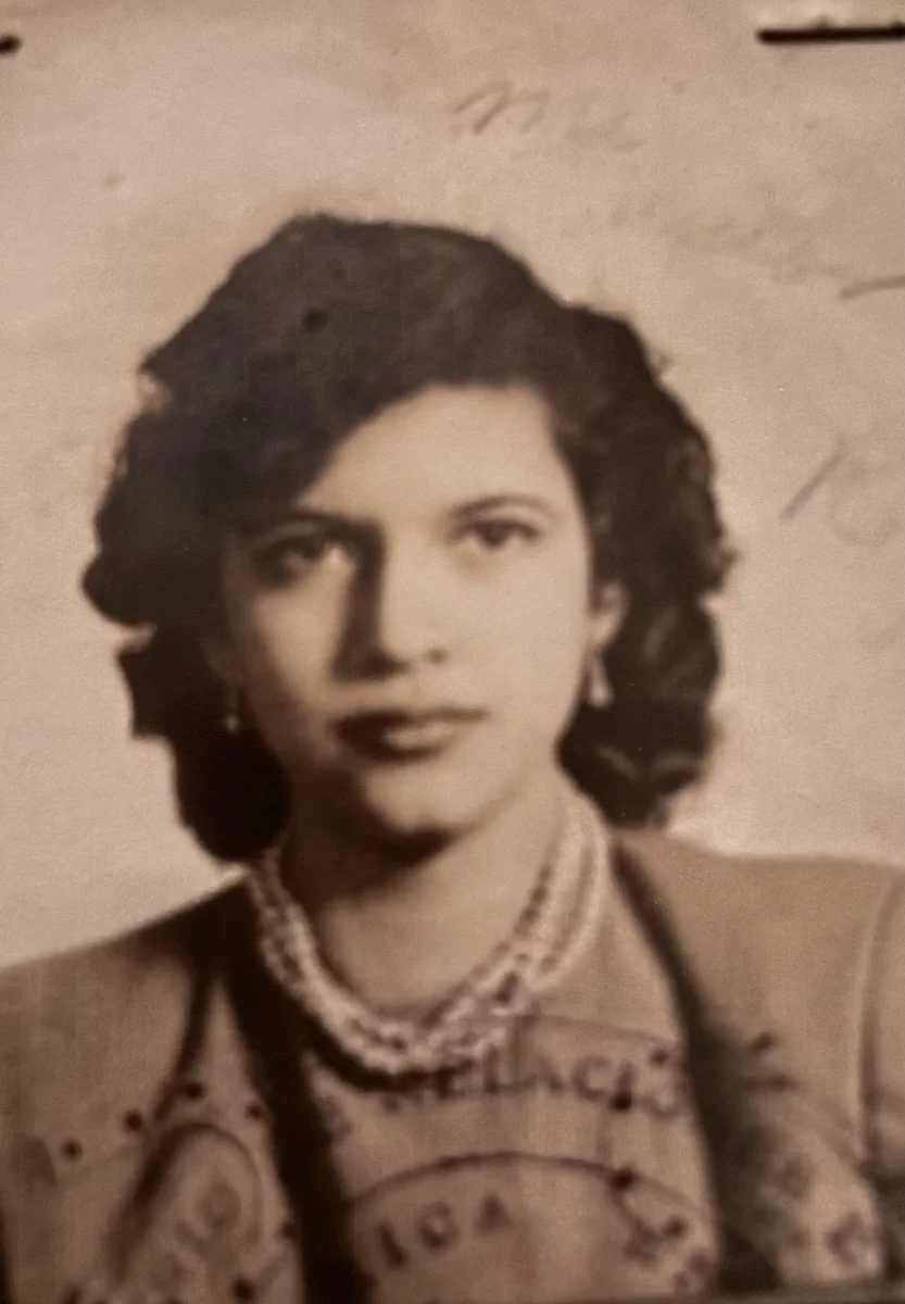 Historical black and white portrait of a woman with wavy dark hair, wearing a beaded necklace and a traditional dress.