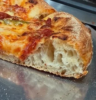 Close-up of a slice of pizza with melted cheese, pepperoni, and green peppers on a metal tray.