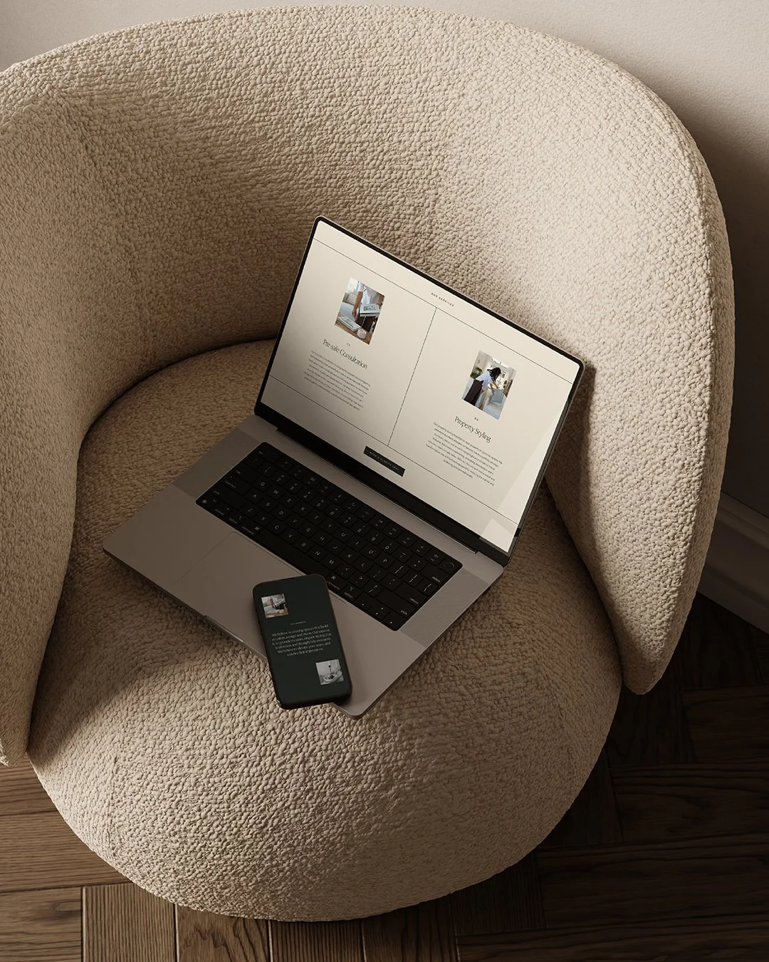 A laptop and smartphone displaying similar webpage content on a cream-colored, textured armchair with wooden flooring.