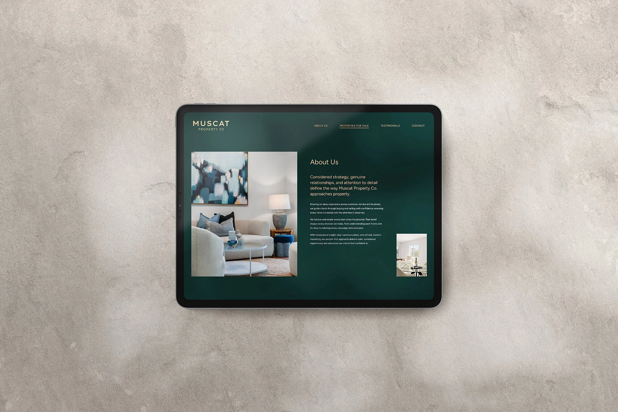 A tablet on a concrete surface displaying a real estate website with images of a living room and interior space.