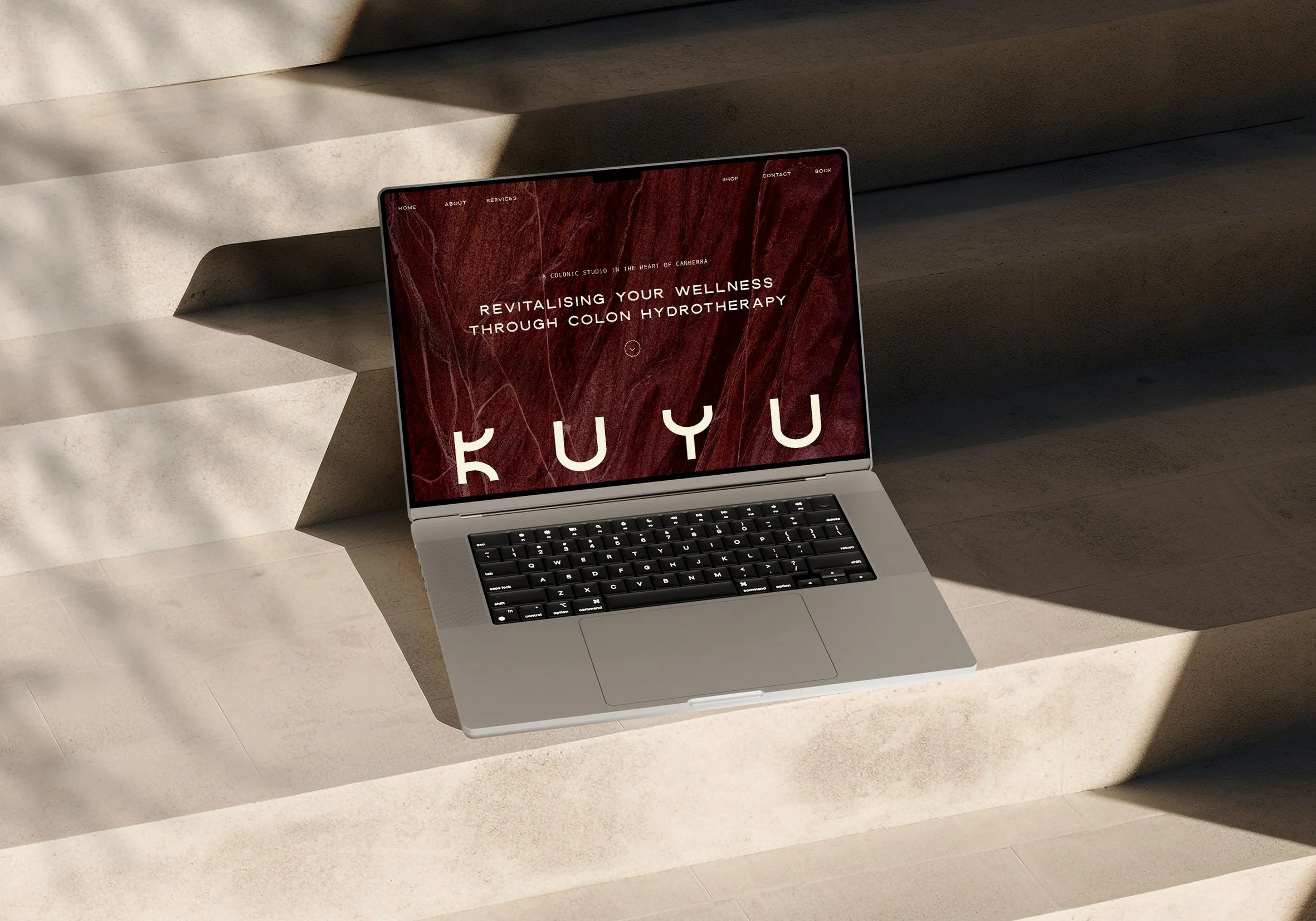 A laptop on a light-colored surface displaying a website for wellness and colon hydrotherapy with a red marble background and menu options at the top.
