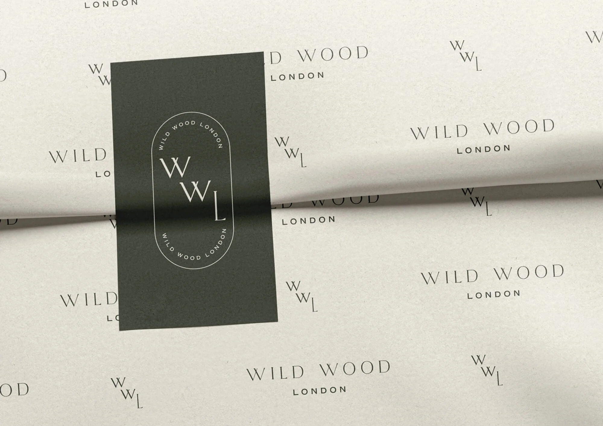 Close-up of white paper packaging with repeated black text 'WILD WOOD LONDON' and a black vertical label featuring the same text in a circle and a large 'WWL' in the center.