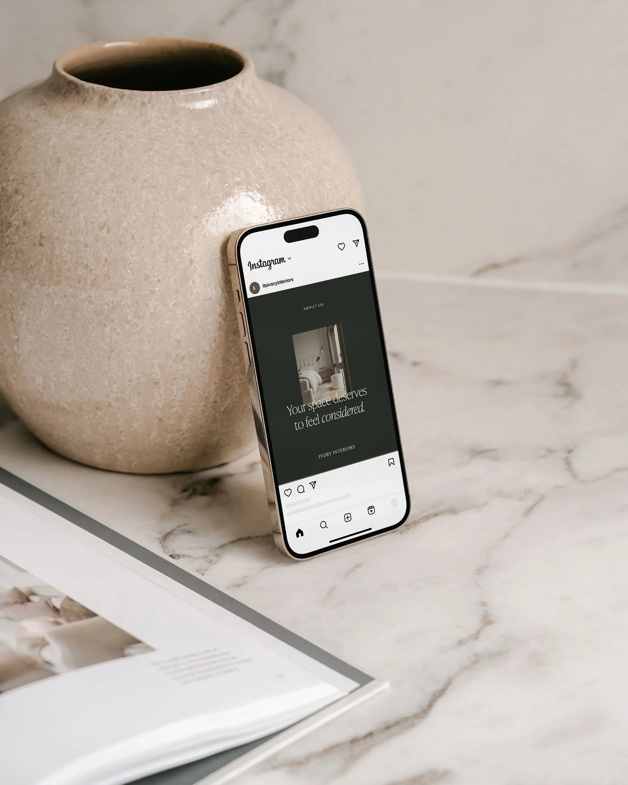 A smartphone displaying an interior design website, resting against a large beige textured ceramic vase on a white marble surface.
