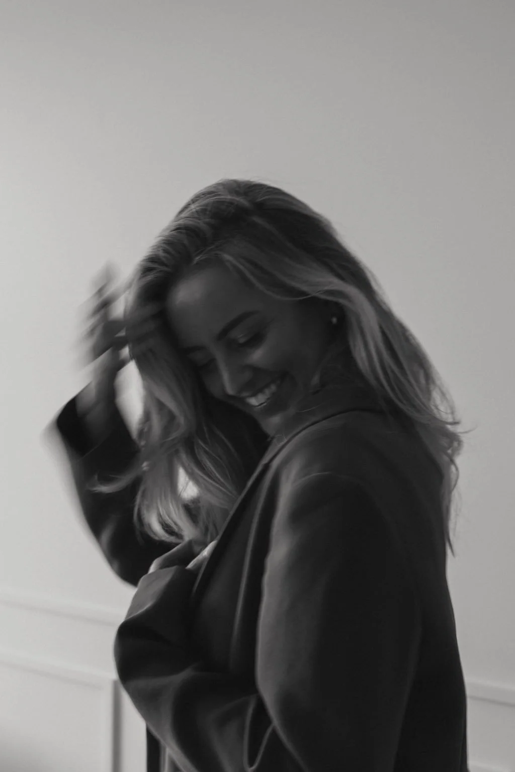 Black and white photo of a woman smiling while touching her hair, wearing a leather jacket.