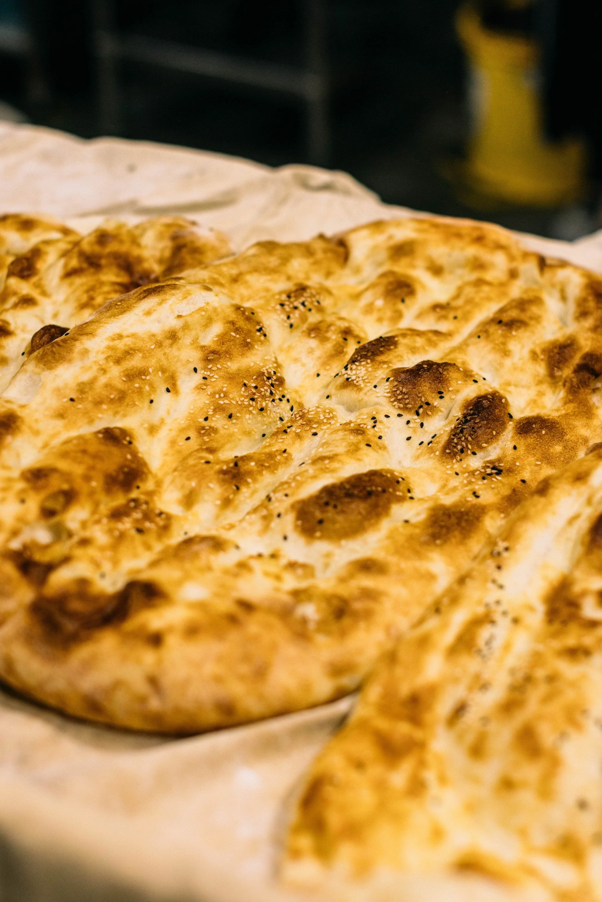 Close-up of freshly baked bread with a golden-brown crust and sesame seeds on top, resting on parchment paper.