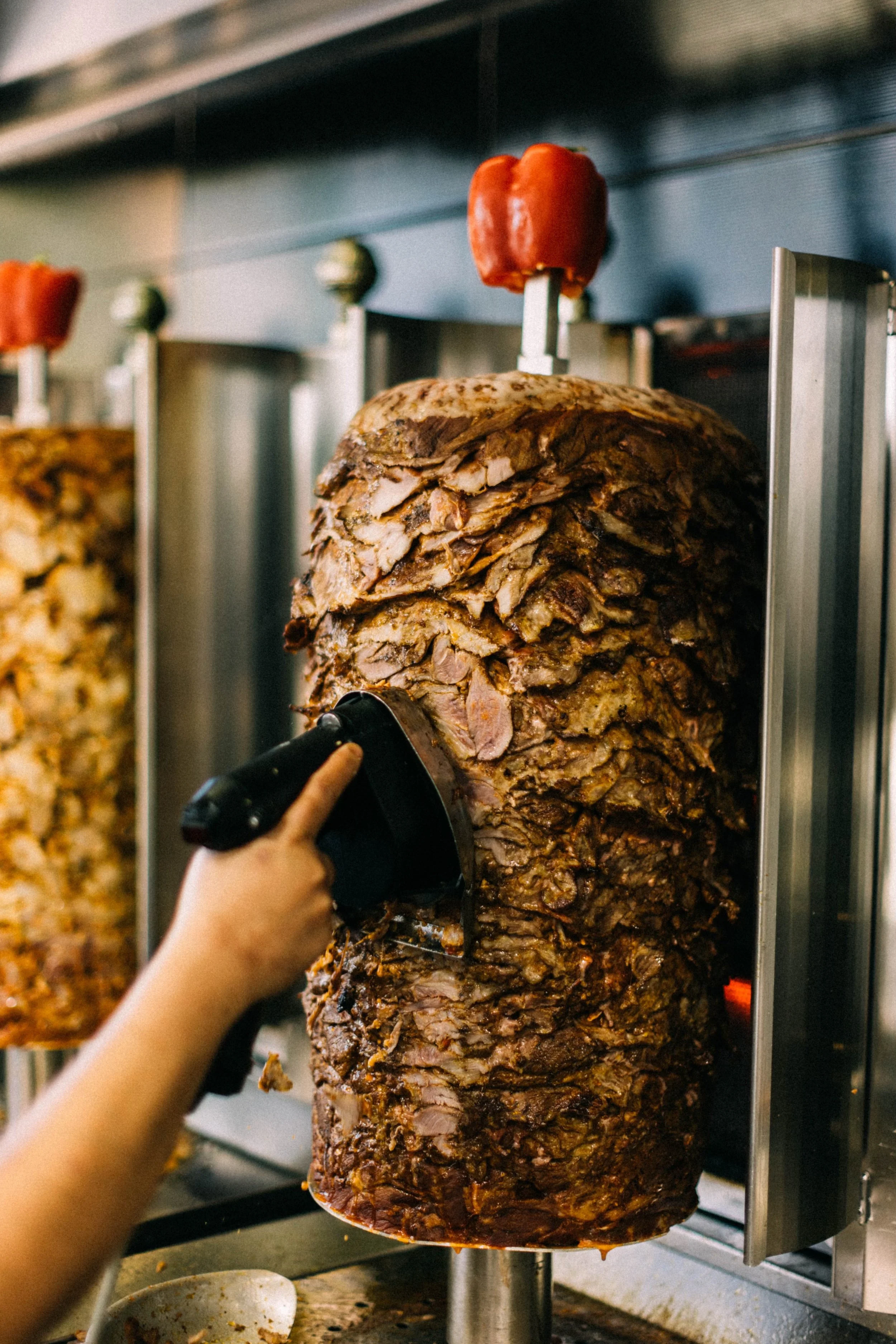A person is carving roasted meat from a vertical spit at a restaurant or restaurant-like setting.
