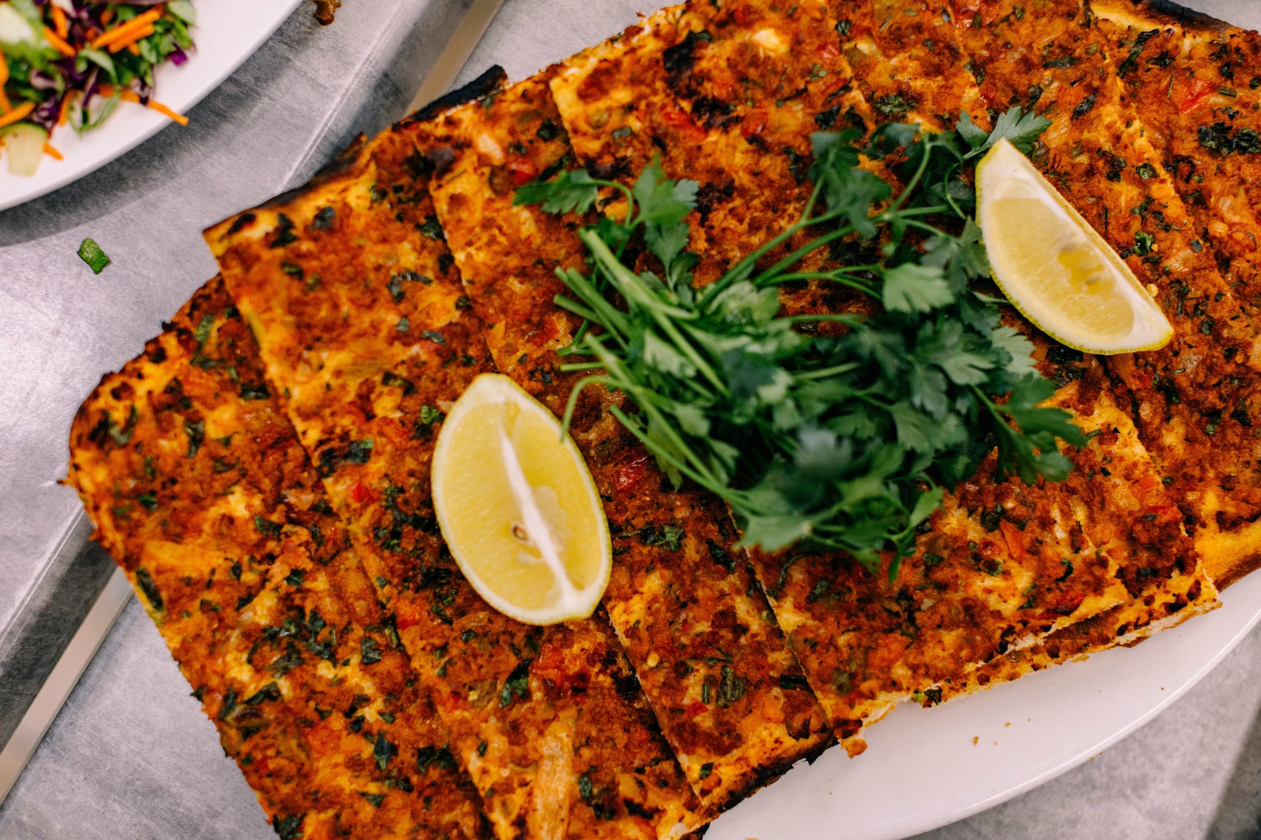 A cooked salmon fillet topped with herbs and seasoning, garnished with fresh parsley and lemon wedges, on a white serving platter.